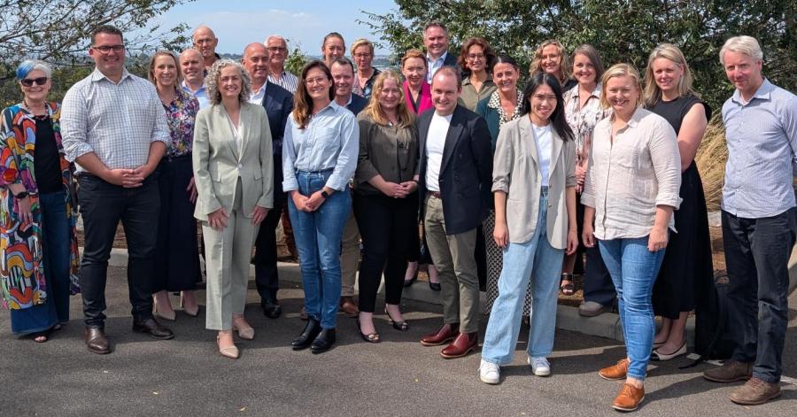 A group of colleagues gathered together outside under blue skies and trees