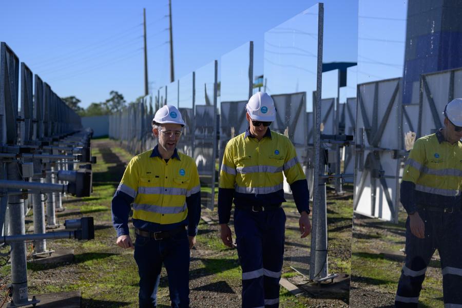 Two men walk between mirrored solar panels