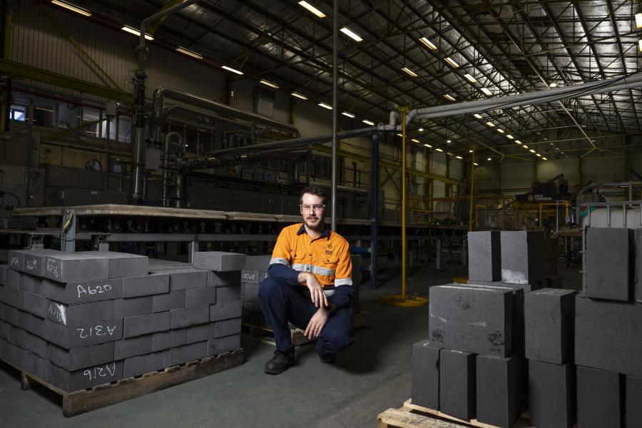 Man in high-vis vest and safety glasses crouching in a factory surrounded by patented MGA Blocks