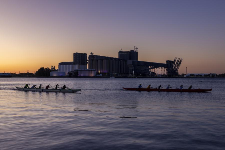 Two rowing boats with rowers skim past the Port of Newcastle in dawn light