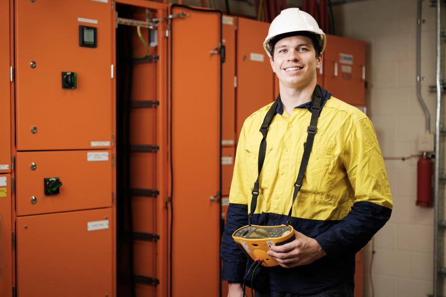 A young tradie in a white hard hat in front of his orange work locker