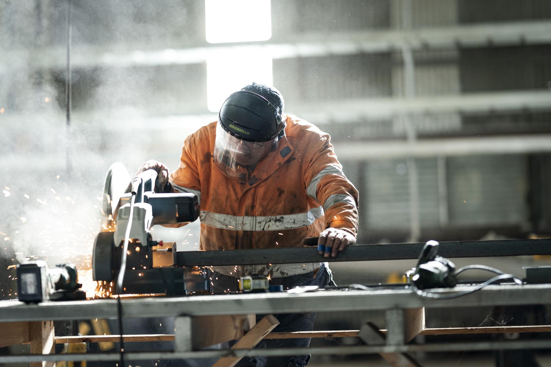 A Worker in high-vis safety gear and a protective mask operates a metal-cutting machine
