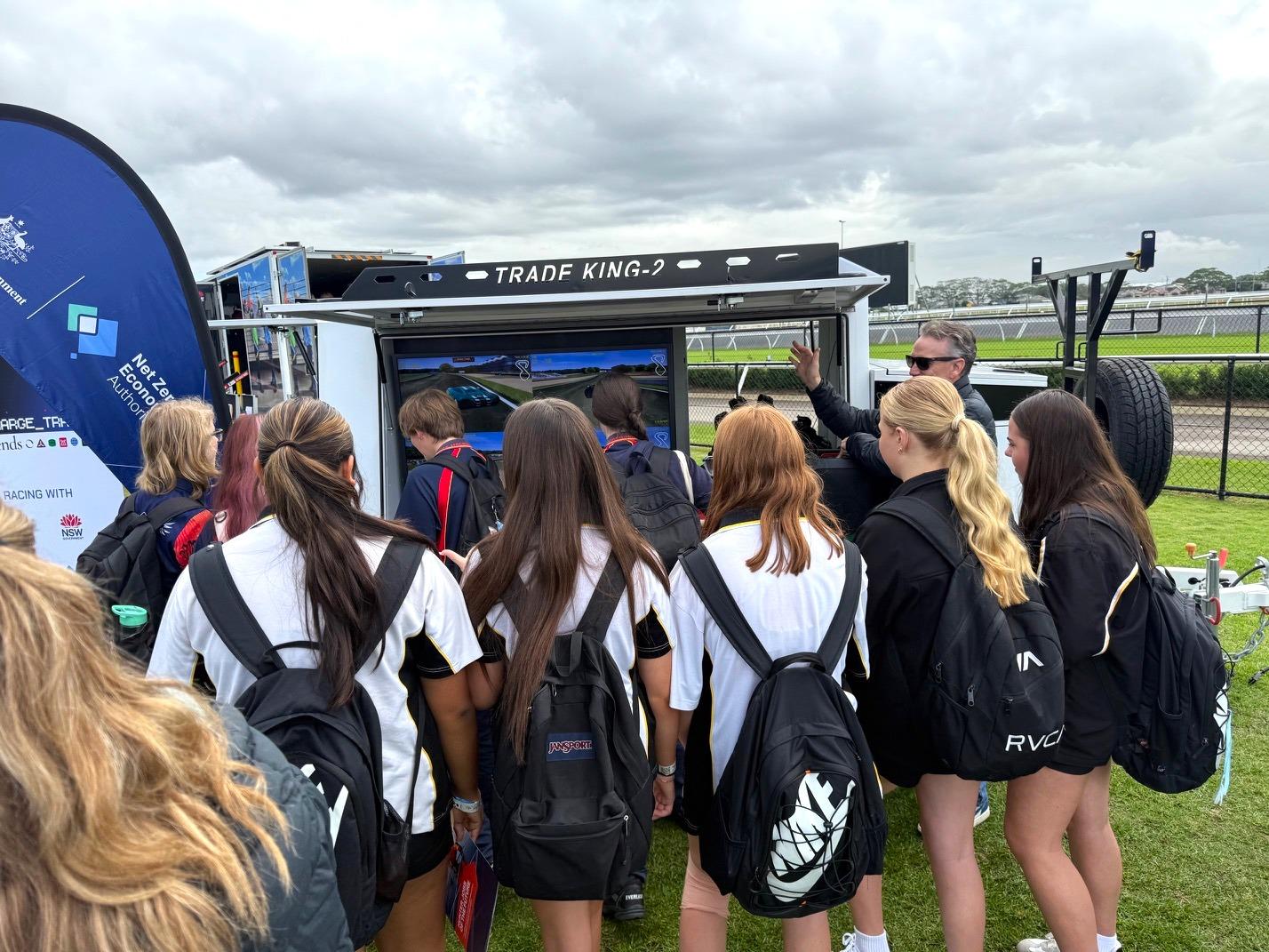 A group of students with backpacks watching a mobile screen display