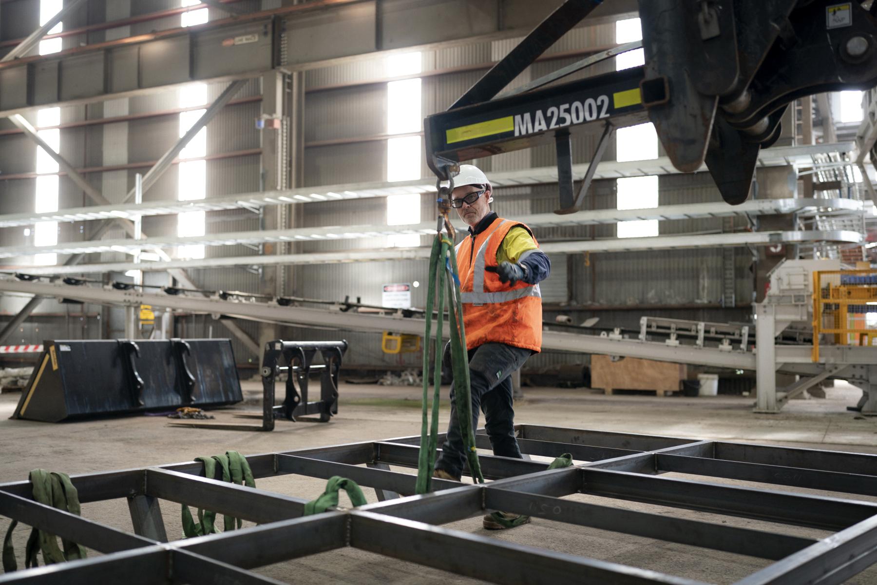 Man in hi-vis safety gear tying a metal structure to a lowered crane