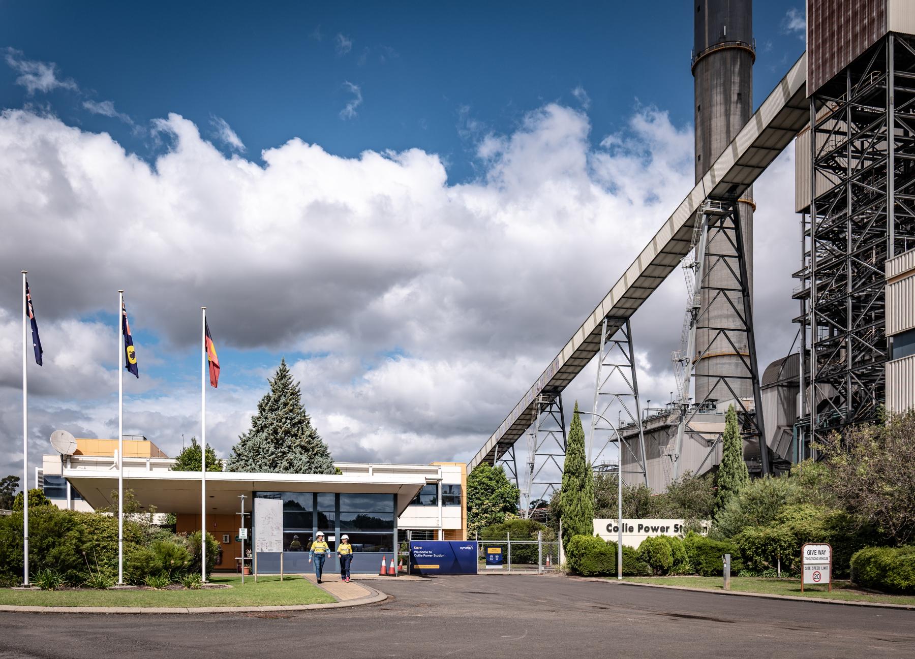 Two workers in hi-vis gear walk in front of Collie Power Station