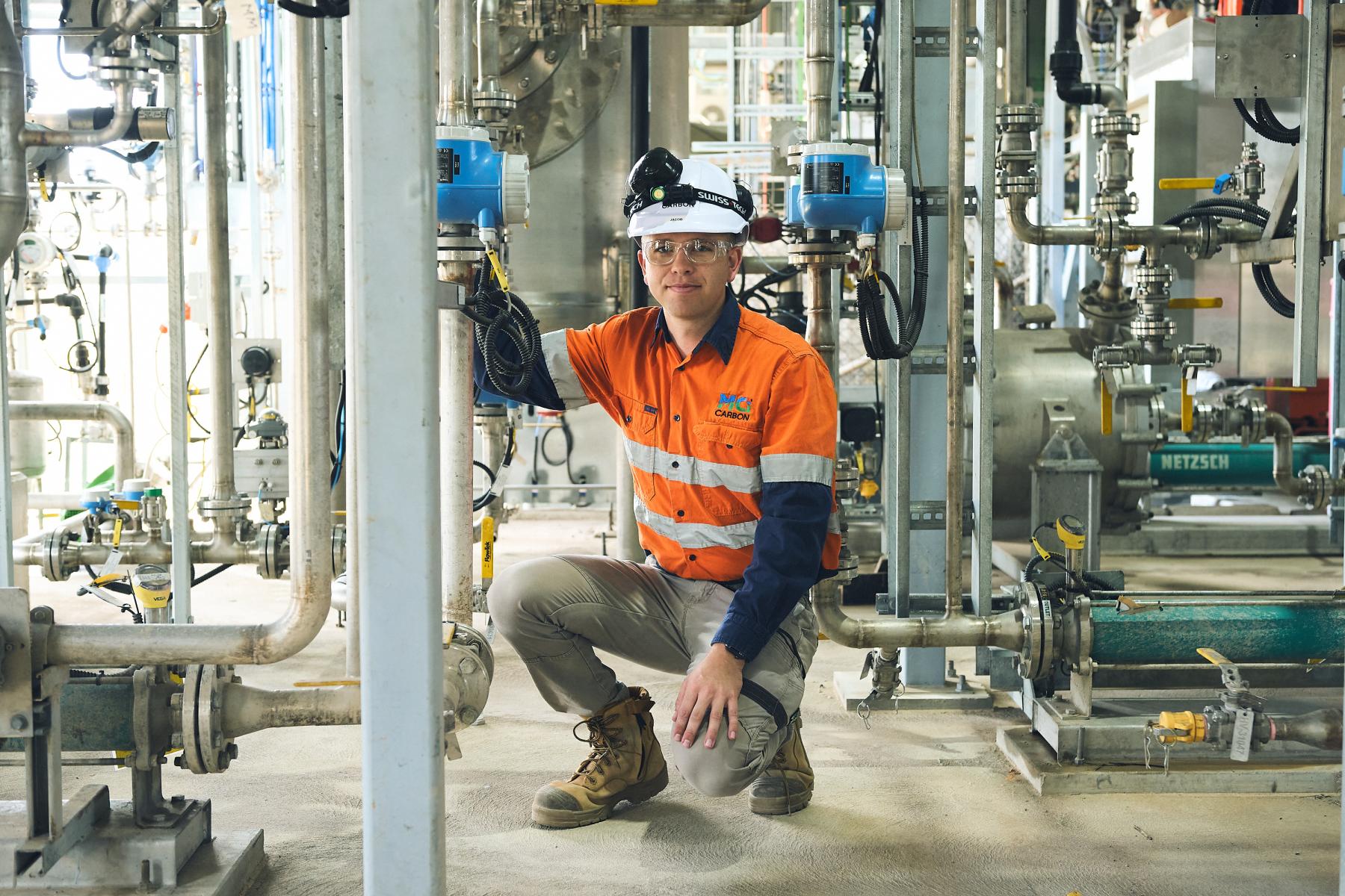 Man in hi-vis safety gear crouched amongst machinery
