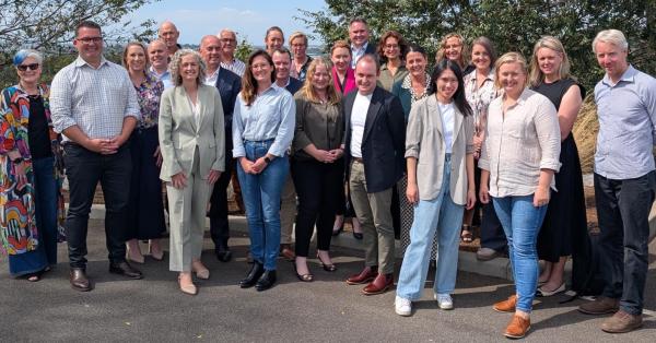 A group of colleagues gathered together outside under blue skies and trees