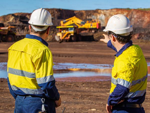 Two workers in high-vis gear pointing towards excavation vehicles
