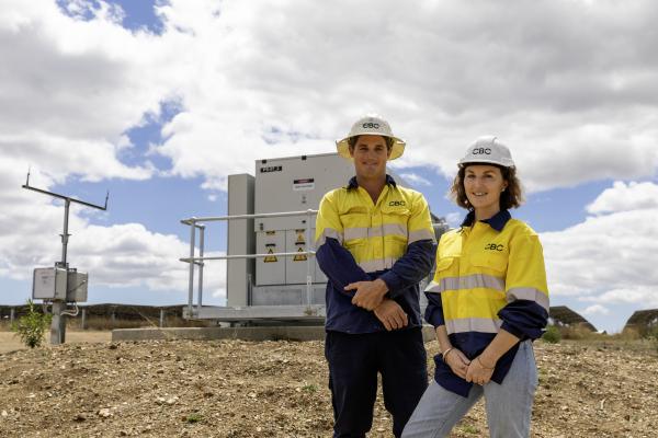 Two workers in hi-vis safety gear standing in front of a solar farm