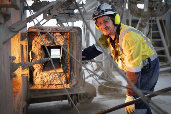 Man in high-vis safety gear smiling while opening a furnace