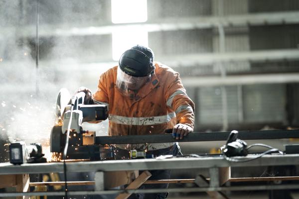A Worker in high-vis safety gear and a protective mask operates a metal-cutting machine