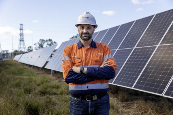 man in high-vis safety gear in a field in front of a solar panel array
