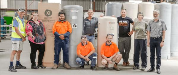Nine people, three in high-vis shirts, standing in front of hot water storage tanks
