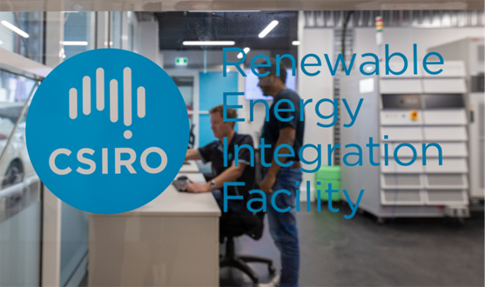 Two researchers working at a desk behind a glass wall imprinted with the CSIRO logo and 'Renewable Energy Integration Facility'