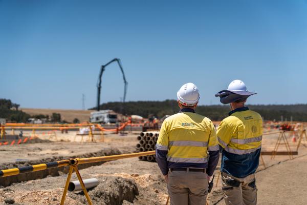 Two construction workers stand in front of a battery construction site.