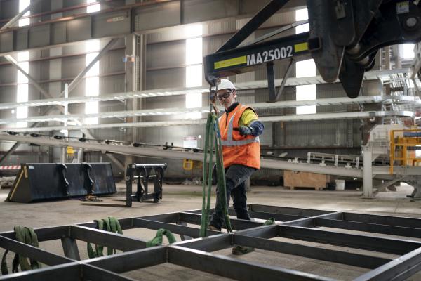 Man in hi-vis safety gear tying a metal structure to a lowered crane